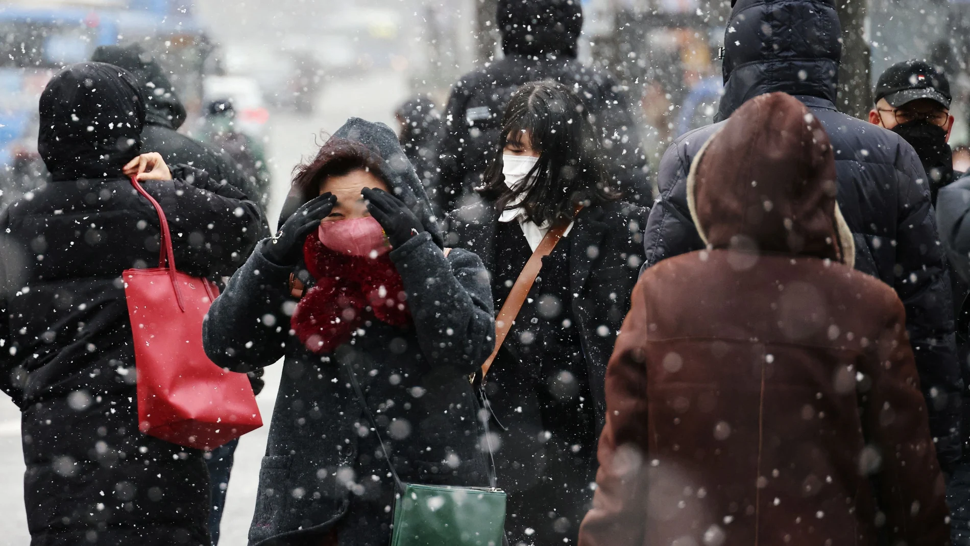 Varias personas caminan en un paso de cebra durante las nevadas, en medio de la pandemia de la enfermedad por coronavirus en el centro de Seúl, Corea del Su