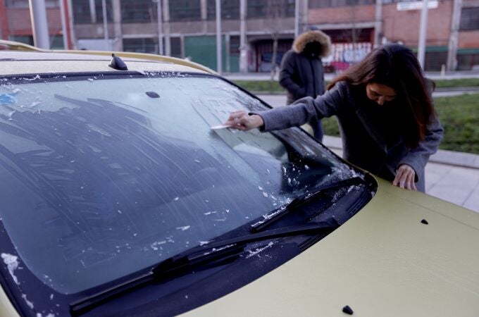 Un mujer retira el hielo de su coche tras la fuerte helada caída esta madrugada en el interior de España