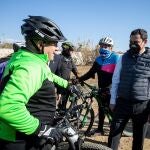 El presidente de la Junta de Andalucía, Juanma Moreno, saluda a unos ciclistas durante el acto de colocación de la primera piedra de las obras de defensa del río Guadalhorce, en Málaga
