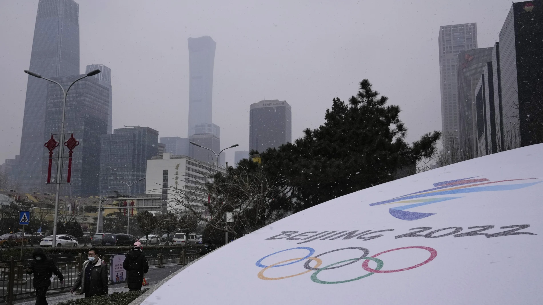 Residents walk past the Beijing Winter Olympics logo near the central business district in Beijing, China, Friday, Jan. 21, 2022. China is limiting the torch relay for the Winter Olympics to only three days amid coronavirus worries, organizers said Friday. (AP Photo/Ng Han Guan)