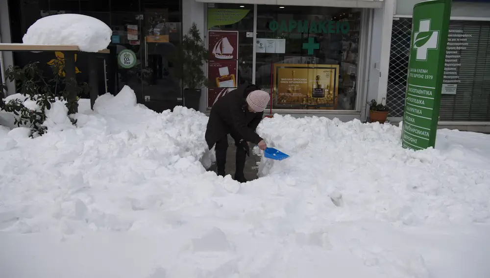 Una mujer retira nieve con una pala en Atenas