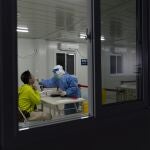 Un sanitario toma una muestra de un hisopo de un hombre en un centro de pruebas de COVID-19 de los Juegos Olímpicos de Invierno de 2022