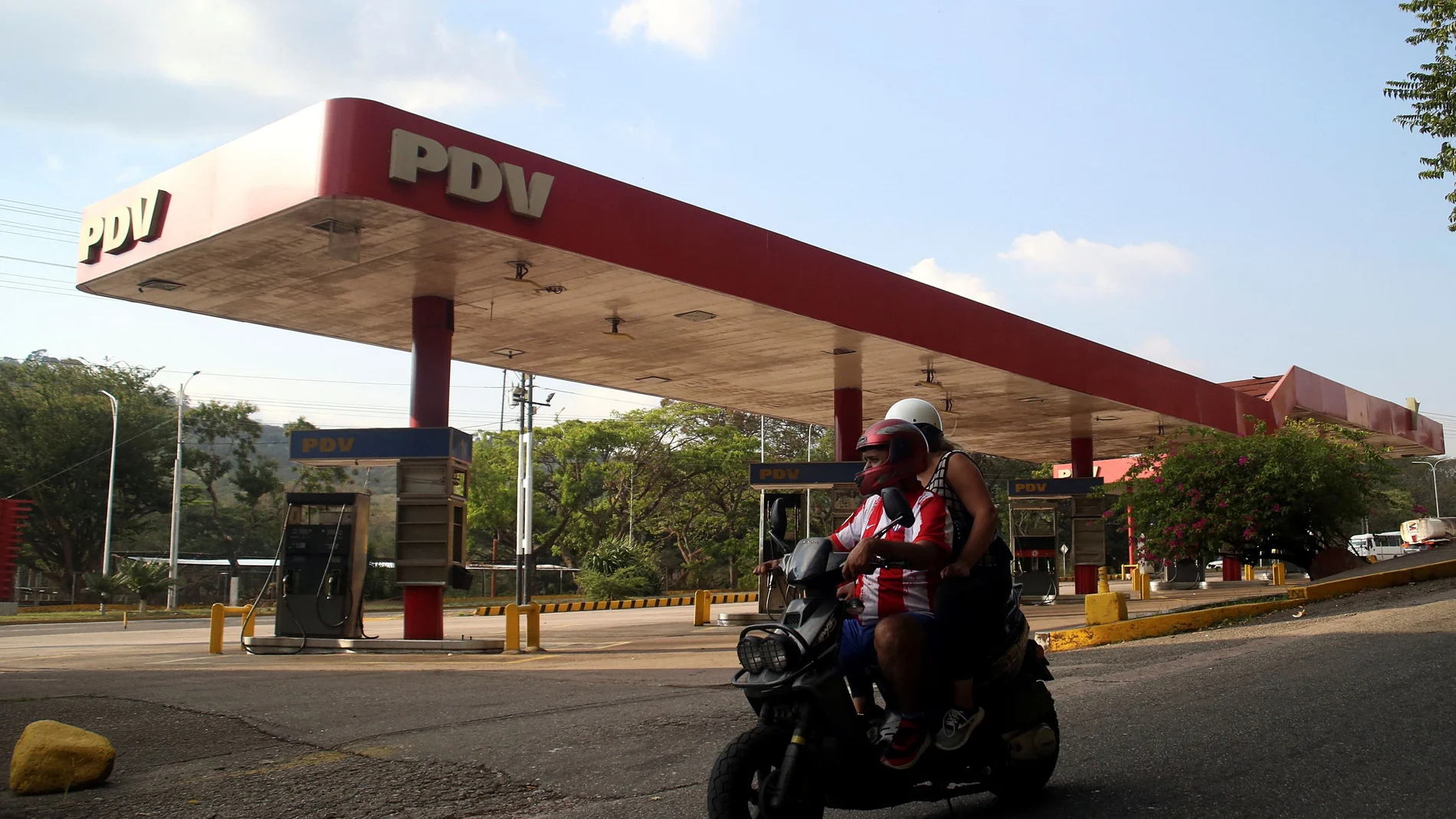 Personas en motocicleta pasan por una gasolinera de la petrolera estatal venezolana PDVSA cerrada por falta de combustible