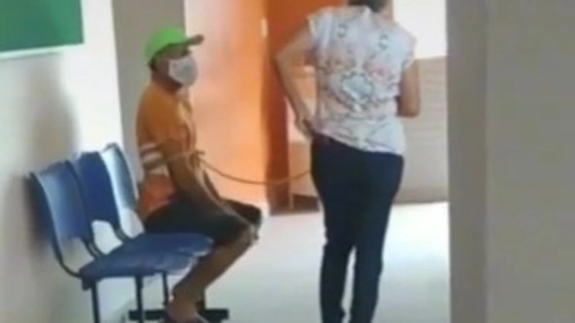 El hombre que llevaba mascarilla, aparece sentado, mientras su mujer está de pie y con una de sus manos lo sujeta con la cuerda.