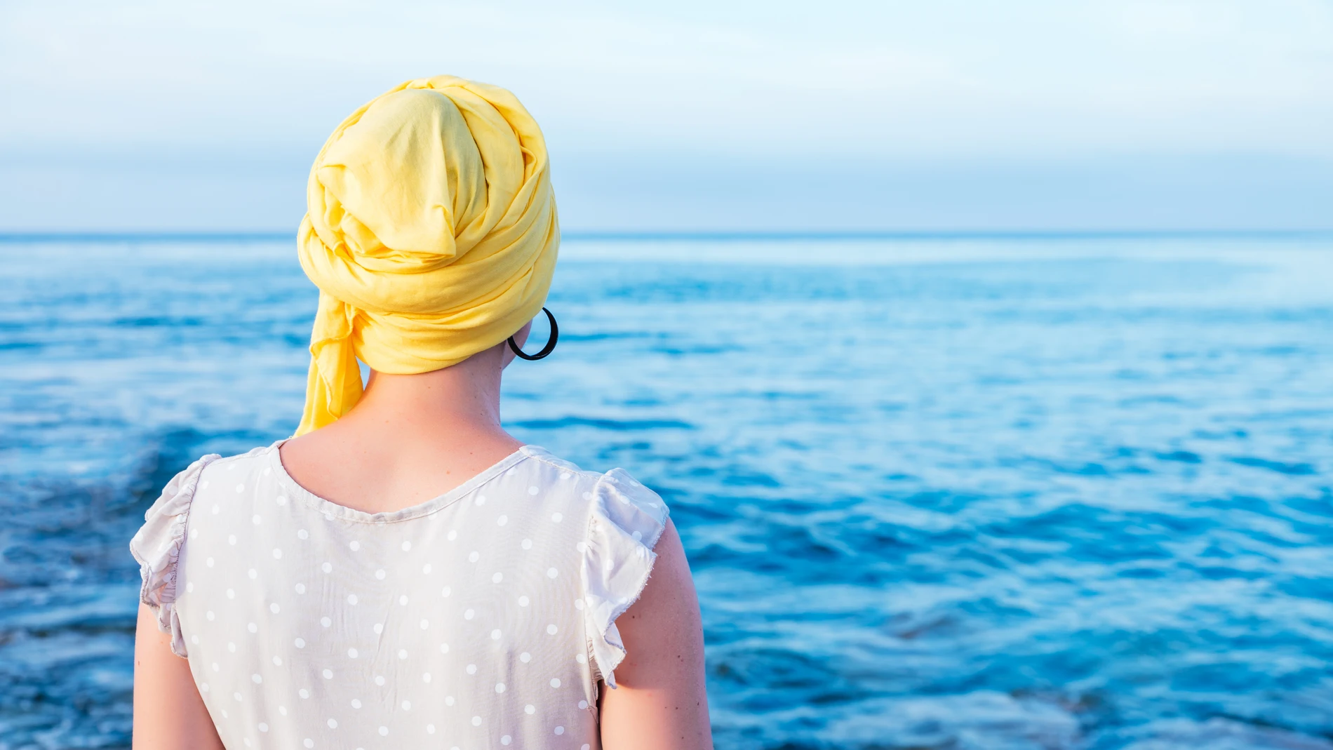 A female with a yellow scarf enjoying the sea view - concept: fight against cancer