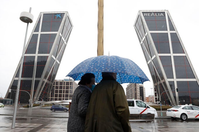 Dos personas se protegen de la lluvia en la Plaza de Castilla en Madrid