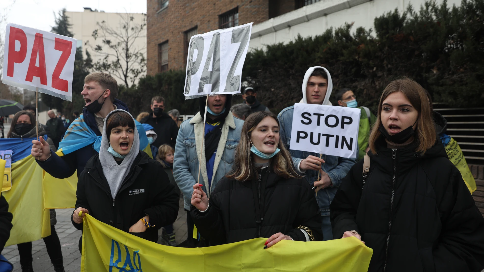 Un grupo de personas con carteles y una bandera de Ucrania participa en una nueva concentración ante la embajada rusa de Madrid