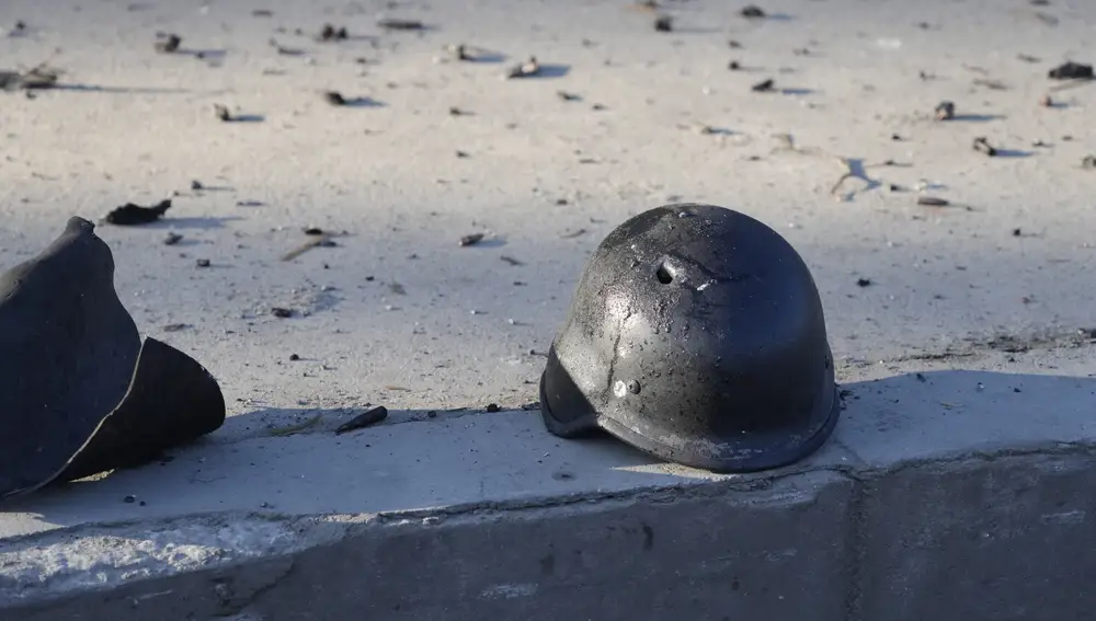 El casco de un soldado con un agujero de bala cerca de los escombros de camiones militares en llamas, en una calle de Kiev