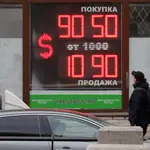 Un hombre camina delante de un panel digital que muestra el tipo de cambio del euro y del dólar estadounidense en una oficina de cambio en San Petersburgo