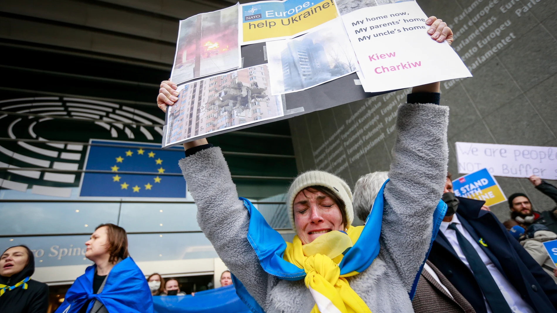 Una mujer llora mientras sostiene imágenes de los bombardeos rusos ante el edificio del Parlamento Europeo en Bruselas