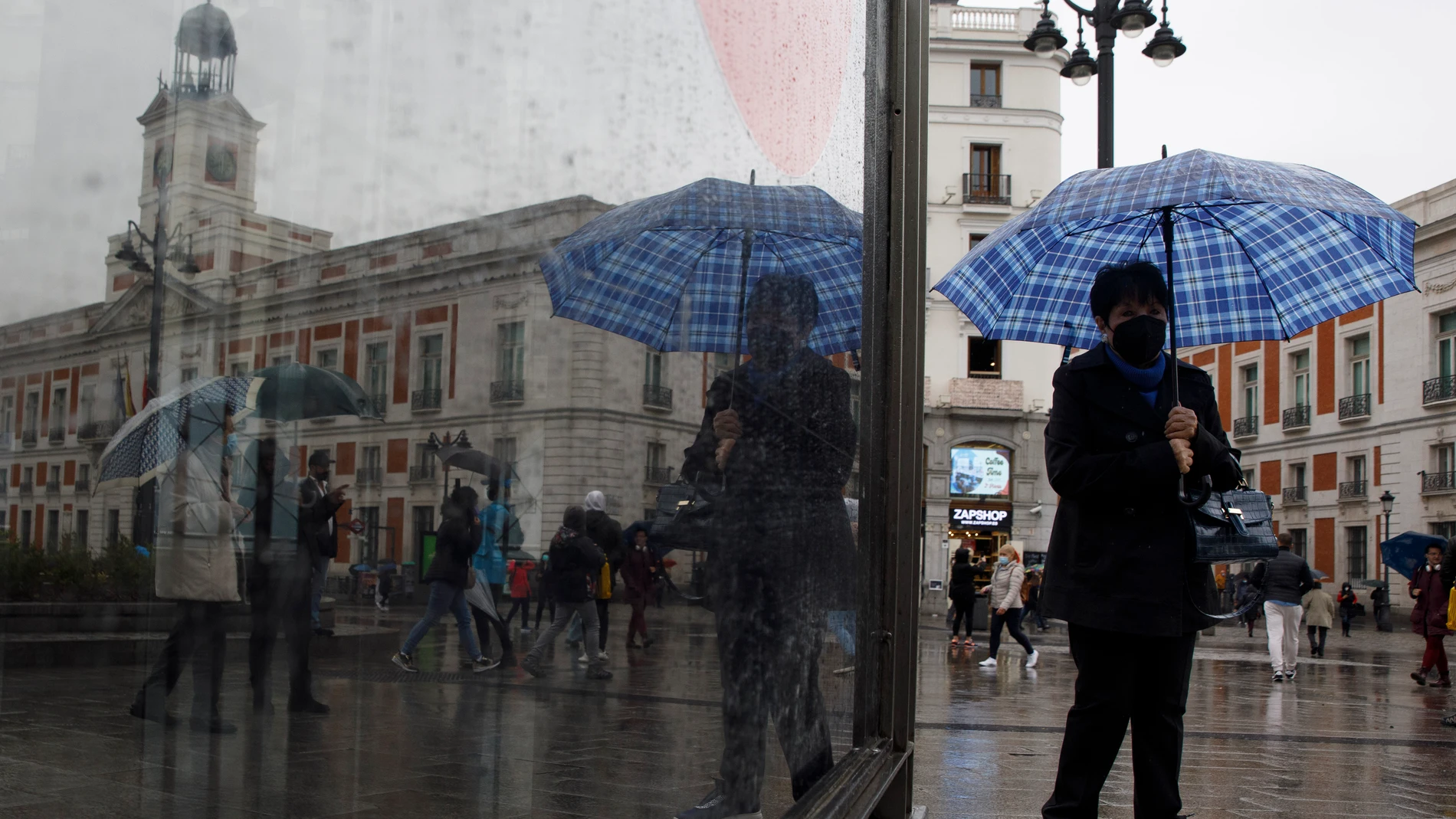 Una persona reflejada en la parada de metro de Sol se protege de la lluvia