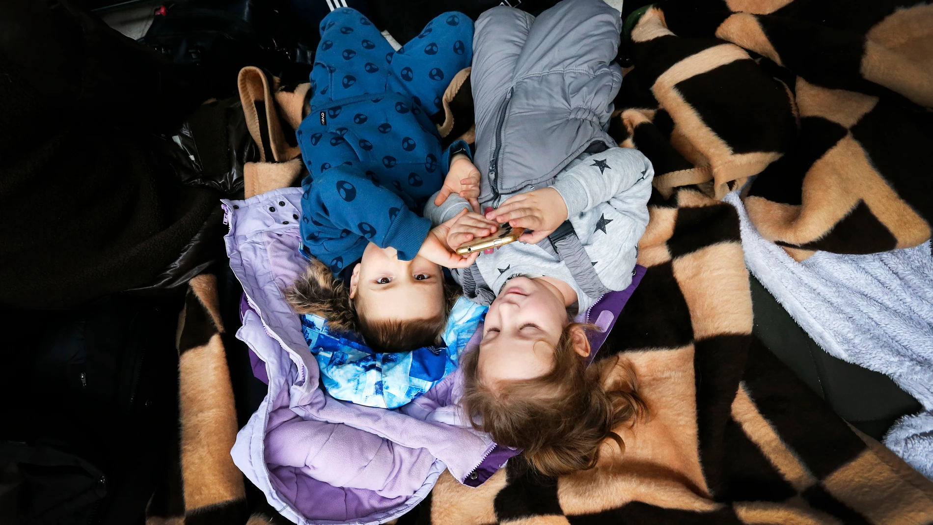 Dos niñas ucranianas refugiadas juegan con un móvil en un centro comercial polaco.