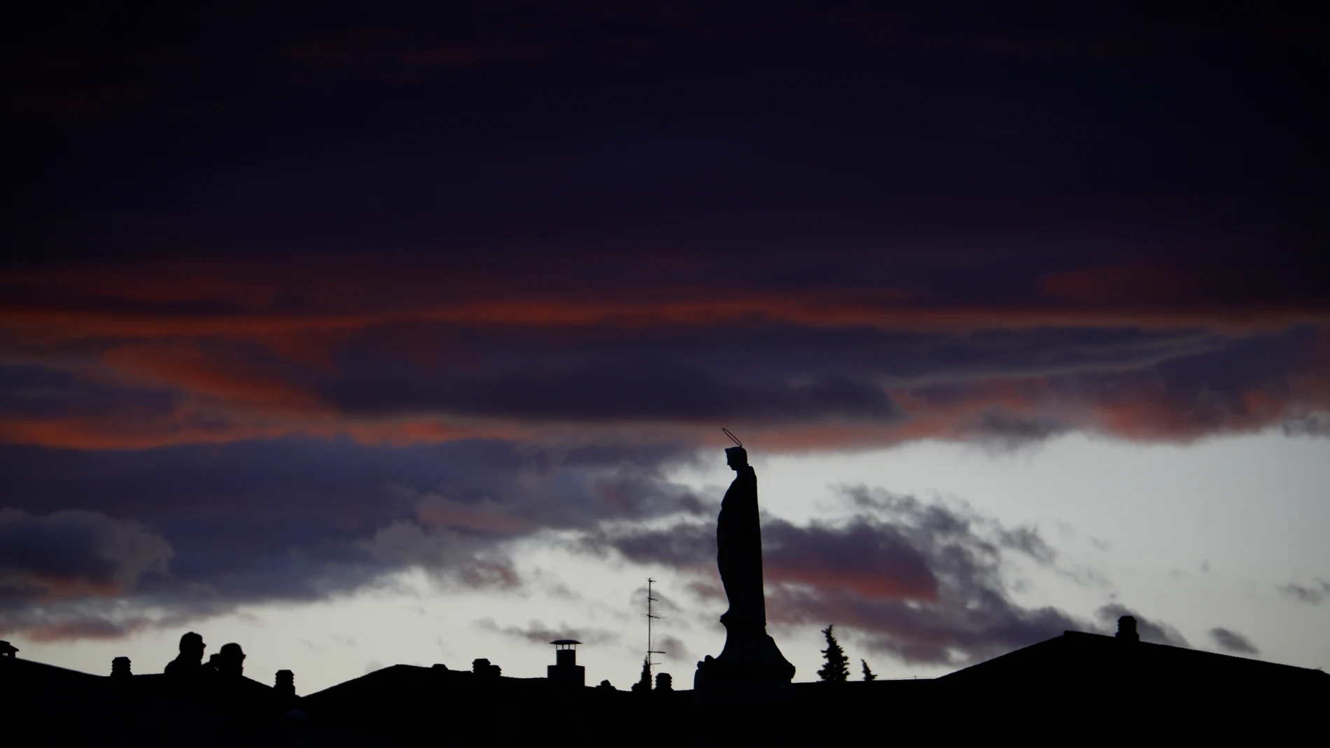 Unas personas observan la estatua del Arcángel San Rafael situada en el puente Romano de Córdoba con cielos muy nubosos. EFE/Salas