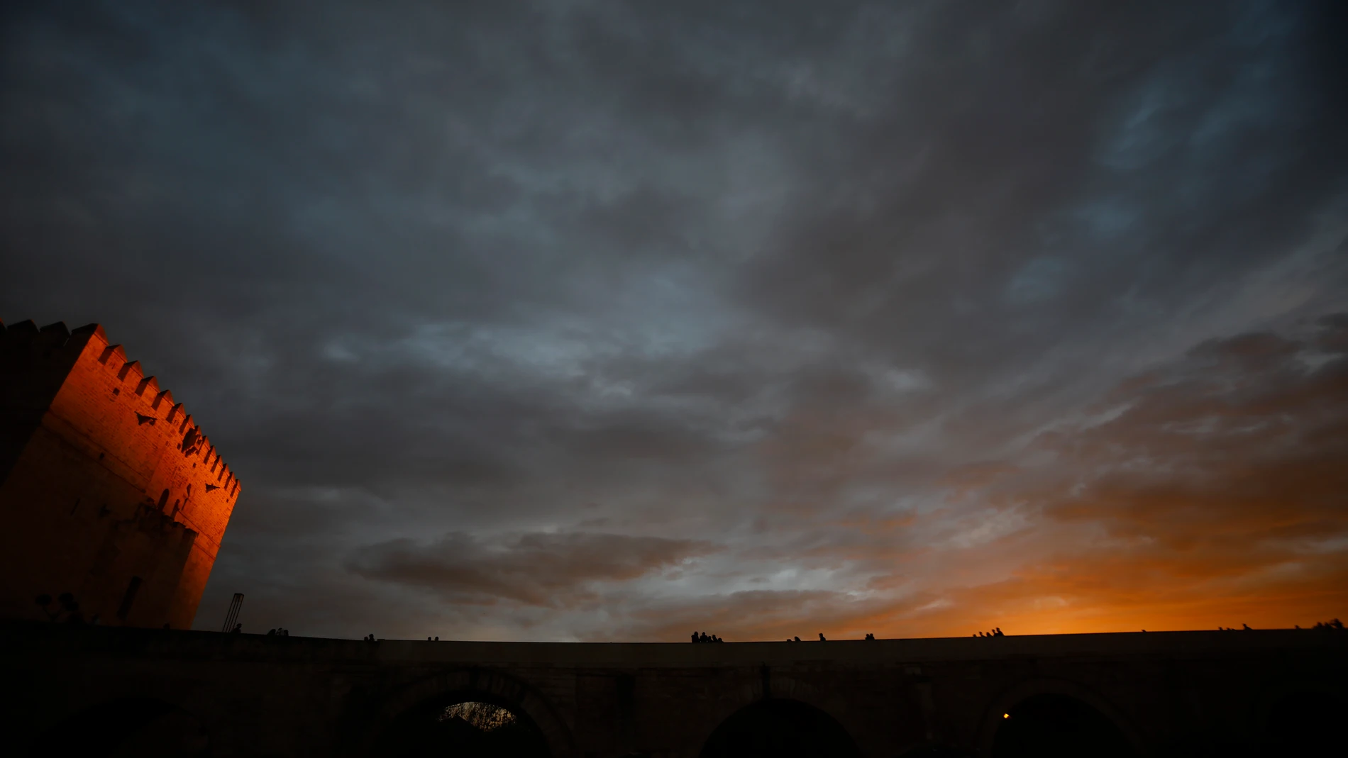 Varias personas caminan por el puente Romano de Córdoba y junto a la torre de la Calahorra en un jornada de cielos muy nubosos. EFE/Salas