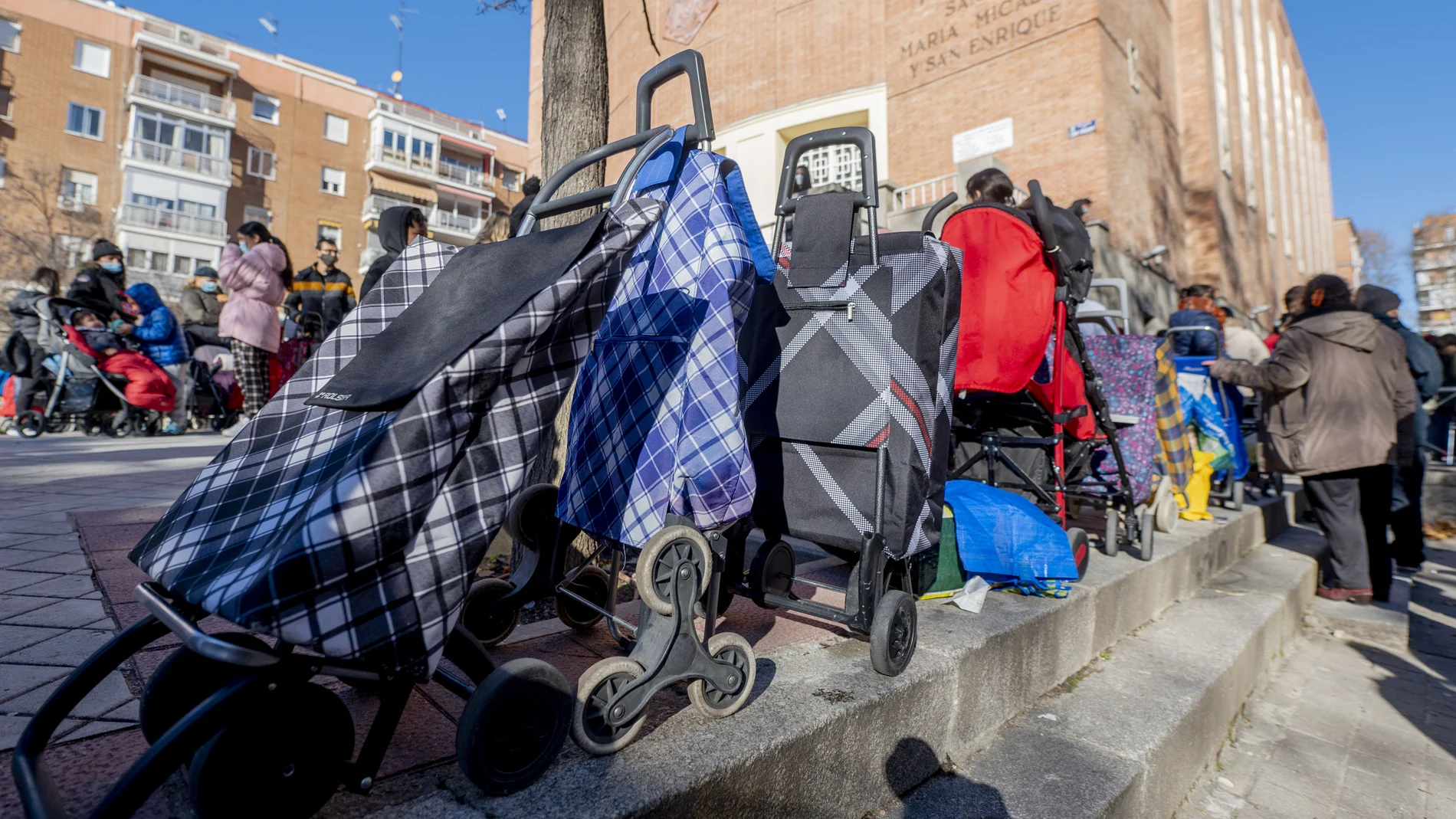 Varias personas hacen cola para recibir alimentos de la Fundación Madrina, en la plaza de San Amaro, en Madrid (España)