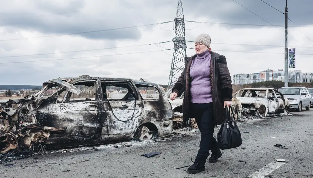 Una mujer camina delante de unos coches quemados en un puente de Irpin (Ucrania) | Fuente: Diego Herrera / Europa Press
