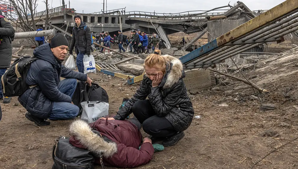 Una mujer junto a otra en el suelo tras la destrucción de un puente en la ciudad de Irpin