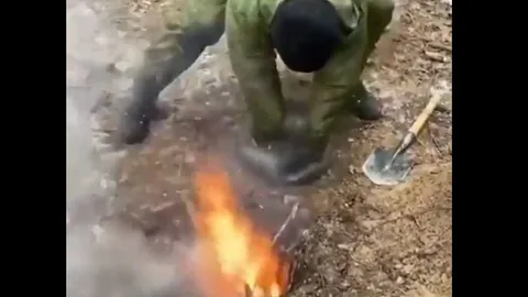 Un soldado ucraniano aviva el fuego usando una bolsa de plástico para introducir aire en el segundo hoyo.