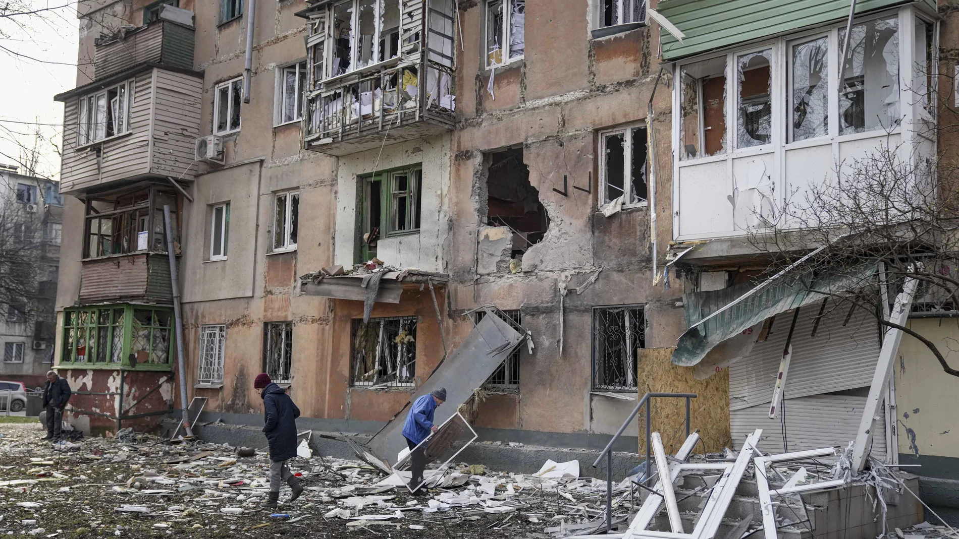 Varias personas junto a un edificio de apartamentos alcanzado por los bombardeos en Mariúpol, Ucrania