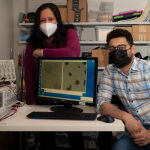 Sibani Lisa Biwal y Kedar Joshi en su laboratorio con una imagen de las partículas magnéticas.