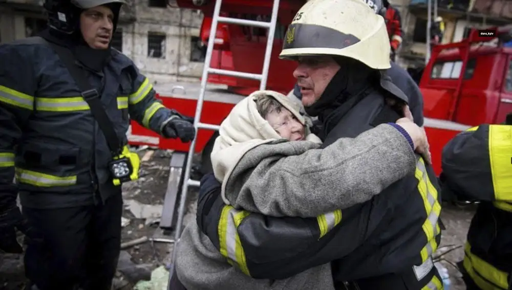 Los bomberos atienden a una anciana tras el impacto de un proyectil en un edificio residencial de Kiev