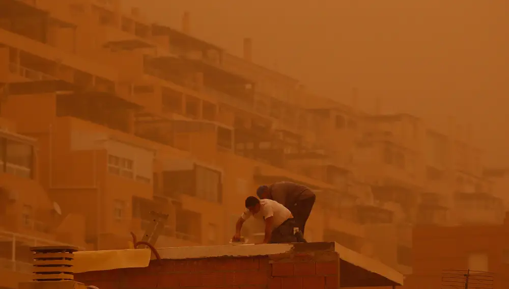 Unas personas trabajan en Aguadulce, Roquetas de Mar ( Almería) que ha amanecido este martes bajo los efectos de la intensa calima que ha cubierto de polvo sahariano buena parte de España.