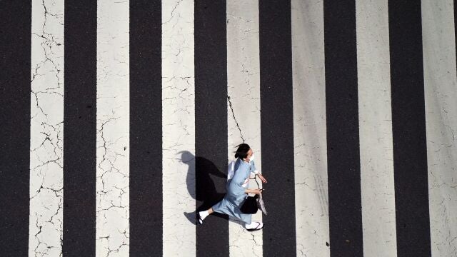 Una mujer con mascarilla vestida con un "kimono" corre por un paso de peatones en el distrito comercial de Ginza