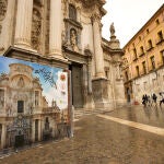 Un hombre camina delante de la fachada principal de la Catedral de Murcia,