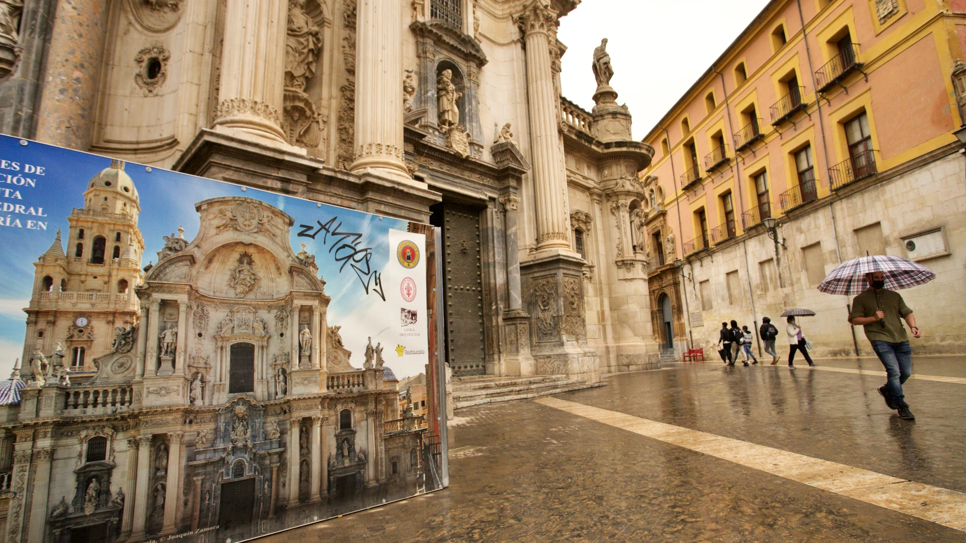 Un hombre camina delante de la fachada principal de la Catedral de Murcia,