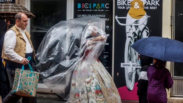 Una fallera se cubre con un plástico de camino a la ofrenda floral a la Virgen de los Desamparados