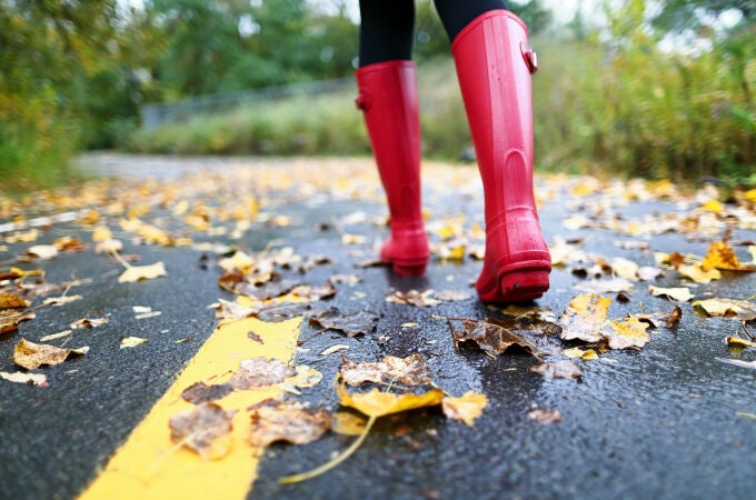 Mujer con botas de agua en una carretera pisando hojas