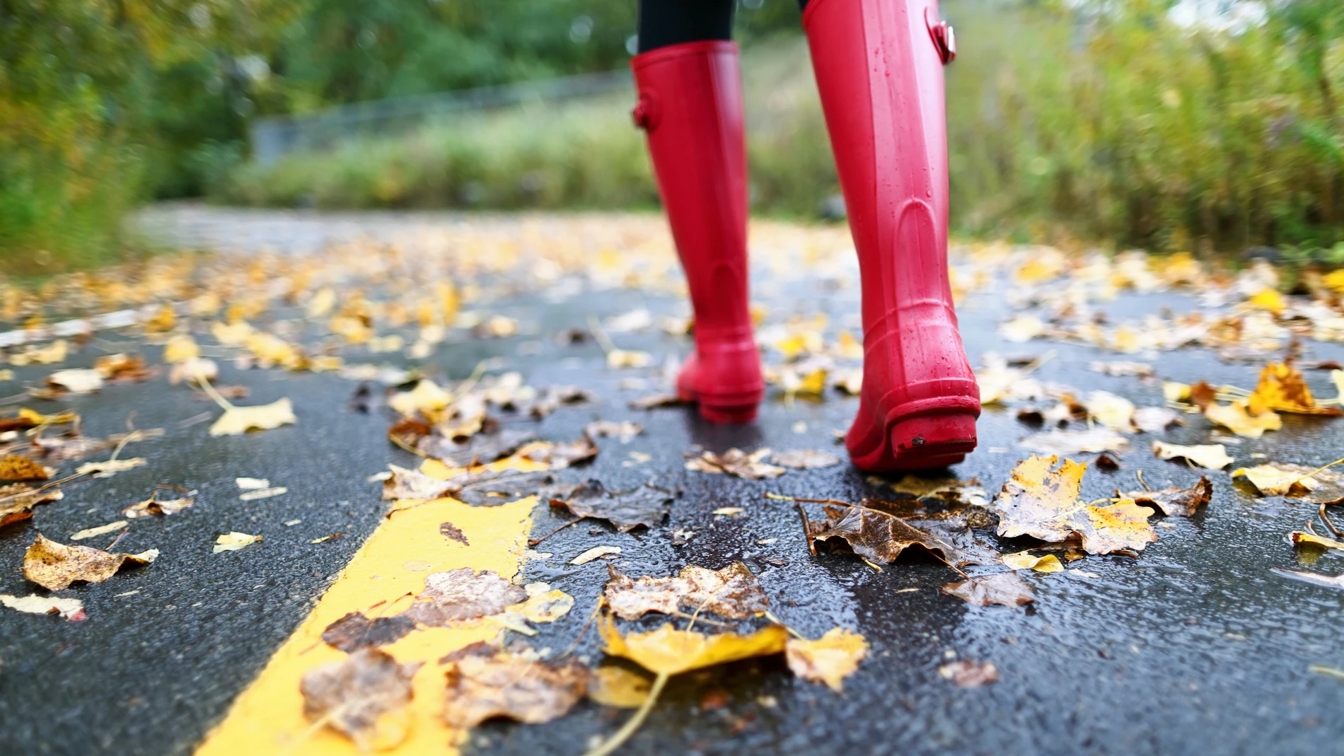 Mujer con botas de agua en una carretera pisando hojas