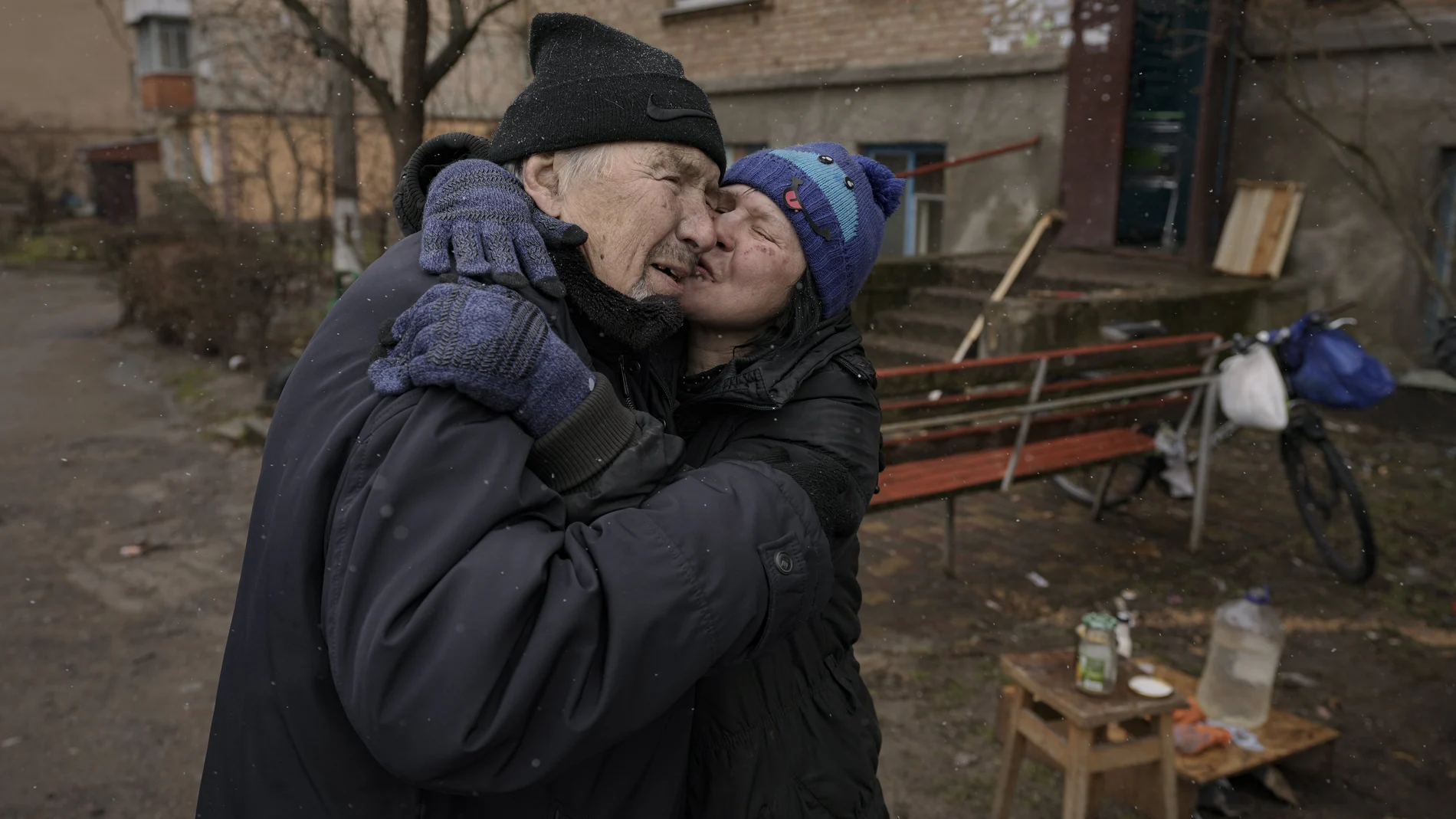 Una mujer besa a un hombre mientras cocina en una fogata fuera de un edificio de apartamentos sin electricidad en Bucha, Ucrania