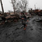 Una mujer pasa por la calle devastada de Bucha en la que se observa la destrucción de los carros de combate rusos