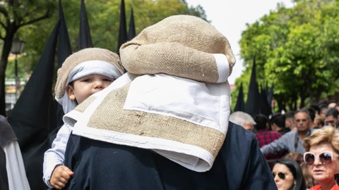 Un costalero de la Hermandad de la Sed de Sevilla lleva en brazos a su hijo, vestido con la misma indumentaria