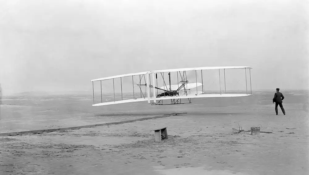 Fotografía original del primer vuelo con motor de la historia el 17 de diciembre de 1903. A los mandos Orville Wright; a la derecha, su hermano Wilbur | Fuente: Dominio Público