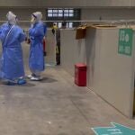 Trabajadores médicos con trajes protectores conversan mientras un residente descansa en el Centro Nacional de Exposiciones y Convenciones el 15 de abril de 2022 en Shanghái.