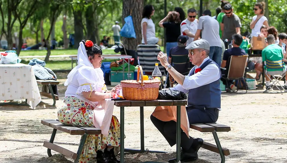 Una pareja vestida con el traje típico madrileño come en una mesa de la pradera de San Isidro.