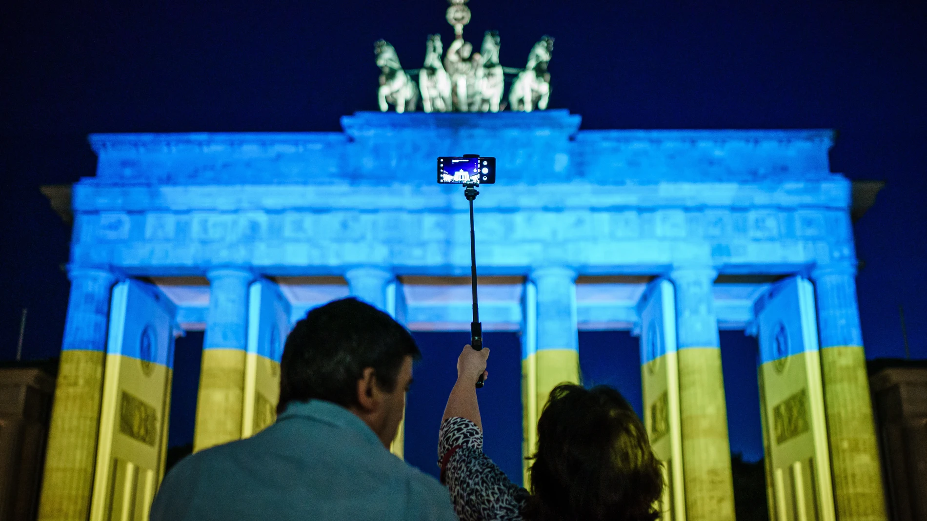 Berlin (Germany), 09/05/2022.- A woman (R) photographs the Brandenburg Gate illuminated in the national colors of Ukraine in Berlin, Germany, 09 May 2022. German Chancellor Olaf Scholz received French President Emmanuel Macron earlier at the Chancellery, where they announced, various buildings all over Europe will be illuminated in the Ukraine colors on Monday evening, among them, the Eiffel tower in Paris. (Alemania, Ucrania) EFE/EPA/CLEMENS BILAN