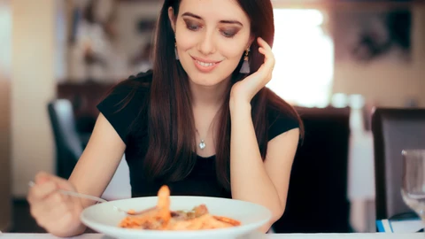 Mujer comiendo pasta con los codos en la mesa | Fuente: Dreamstime