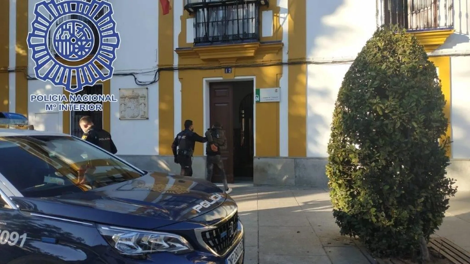 El detenido, custodiado por un policía, entra detenido en la comisaría de Alcalá de Guadaíra
