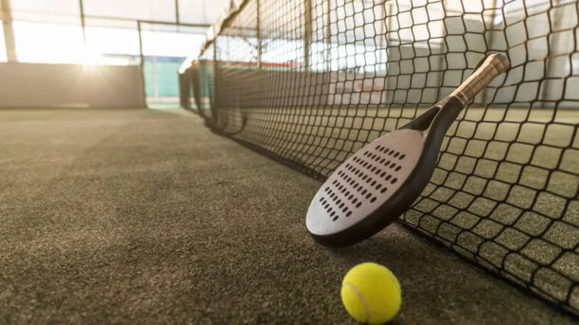 Paddle tennis image of outdoors court, racket, net and ball