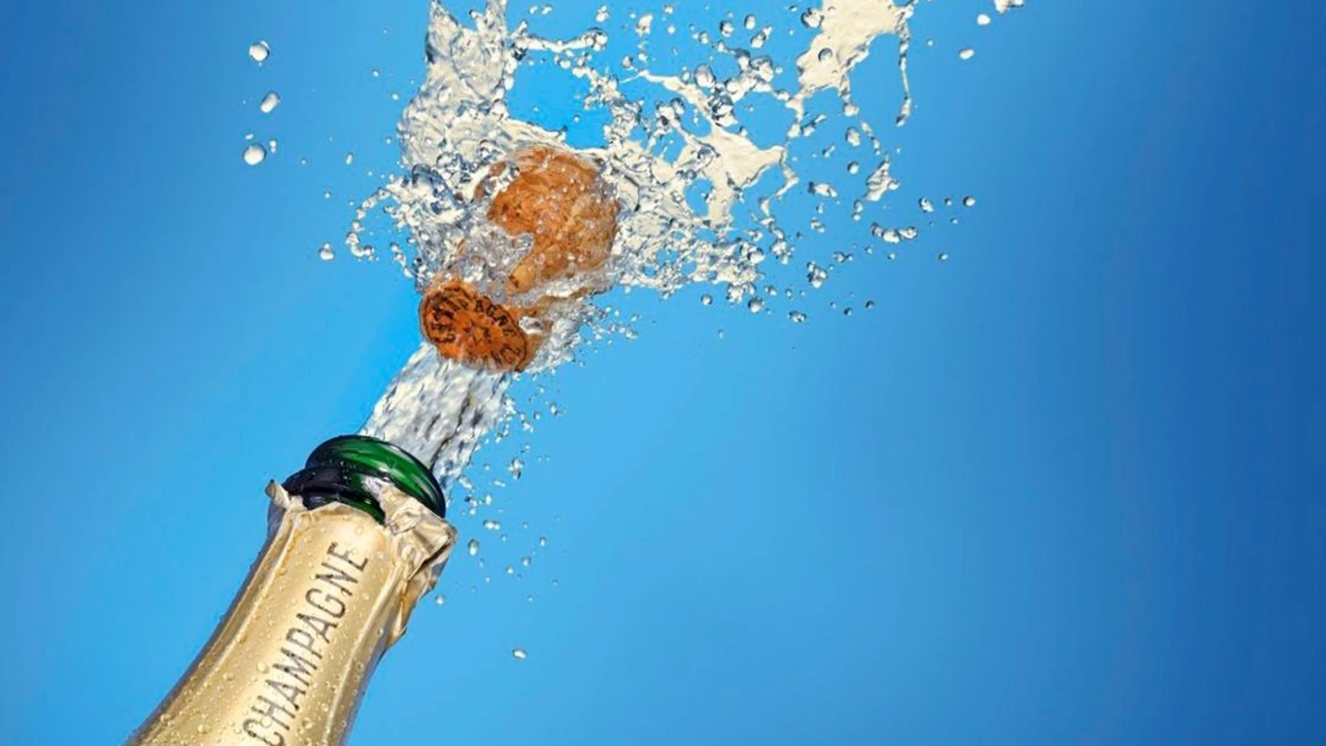 Botella de champán con el corcho saliendo, donde se ven gotas que salen disparadas alrededor del corcho.