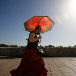 Una mujer se protege con un paraguas de las altas temperaturas mientras pasea por el puente Romano de Córdoba. EFE/Salas