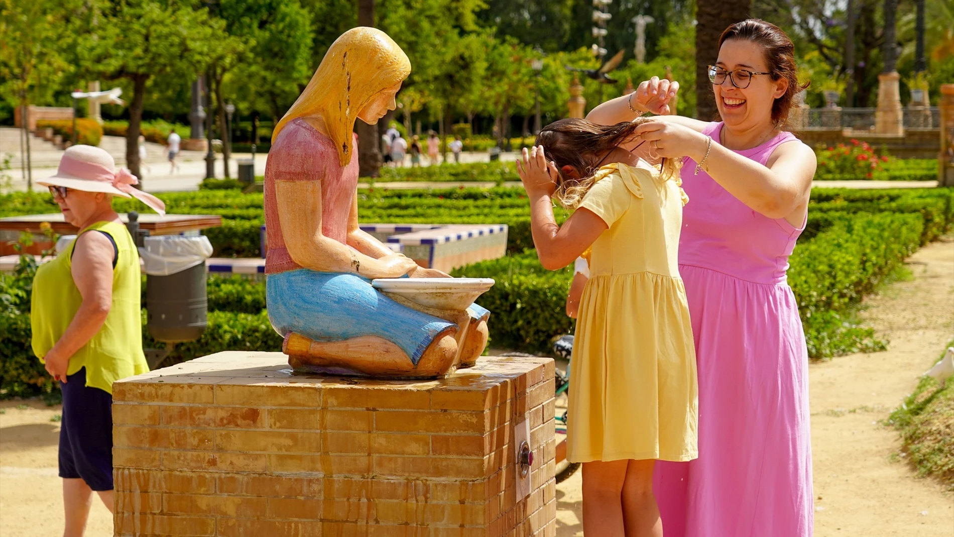 Una madre refresca a su hija en una fuente de el Parque de María Luisa
