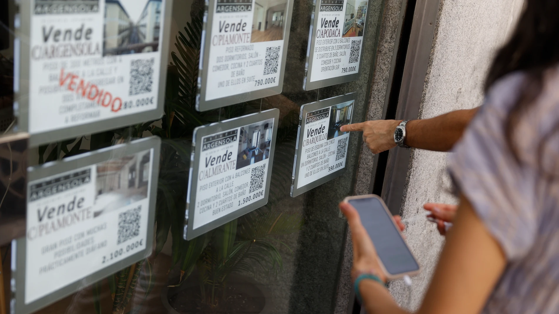 Unas personas se paran delante del escaparate de una inmobiliaria que publicita los inmuebles que gestiona, en el centro de Madrid