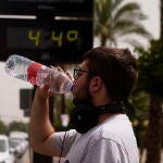 Un joven bebe agua junto a un termómetro de calle que marca 44º en el centro de Córdoba