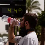 Un joven bebe agua junto a un termómetro de calle que marca 44º en el centro de Córdoba