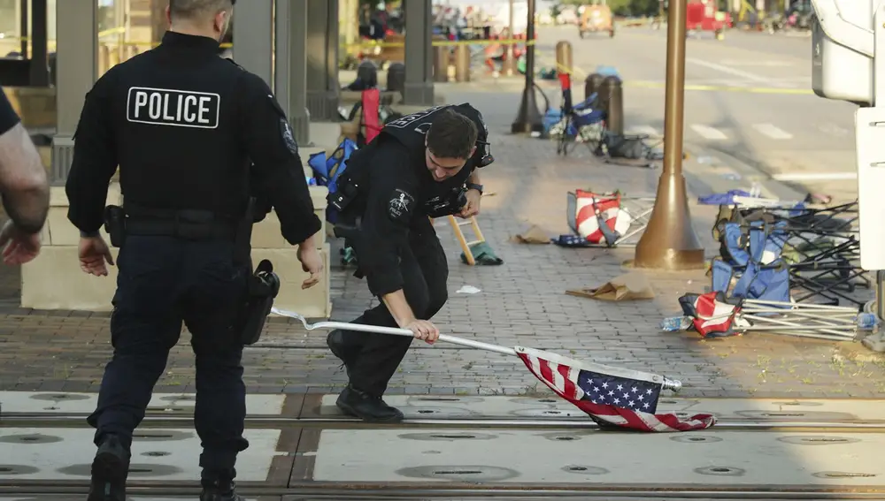 Un policía coge una bandera de EE UU tirada en el suelo tras la estampida por el tiroteo del 4 de Julio