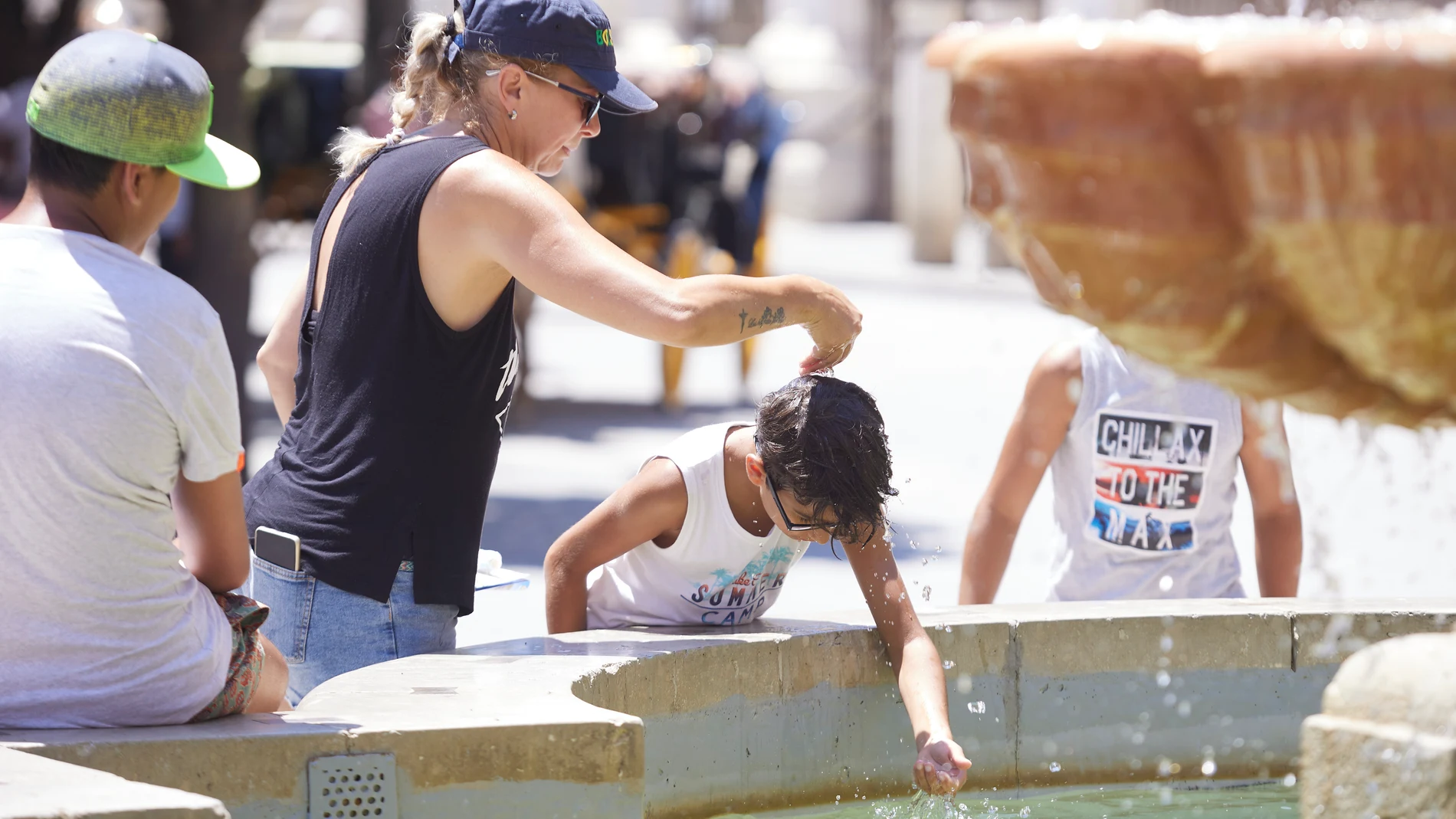 Una madre le echa agua a su hijo, por la cabeza, en la fuente de la plaza Virgen de los Reyes en Sevilla
